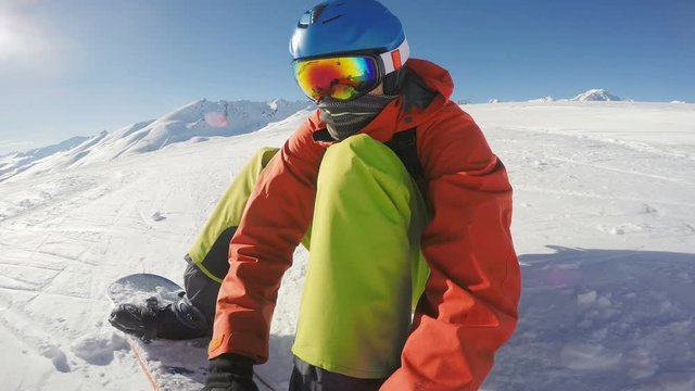 Snowboarder putting his snowboard on and starting to ride down a ski slope face view rotating camera

