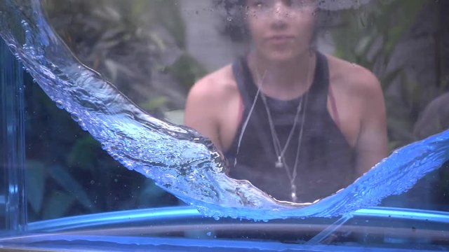 Hispanic woman observing science project, recipient filled with water spinning demonstrating the centrifuge force. Liquid experiment. Slow motion