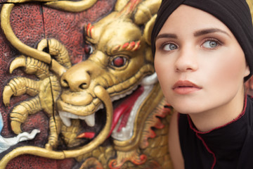 Fashion closeup portrait of young brunette woman with black hat over golden dragon on the wall background