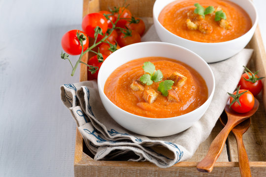 Tomato soup with cream, croutons and parsley on a white wooden table