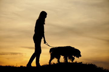 Silhouette of girl and her dog with beautiful sunset background.