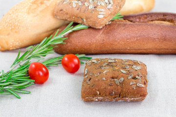 Close up of brown bread with seeds and rosemary and tomato on table with other breads. Healthy morning breakfast.