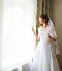 beautiful young bride standing beside a window waiting