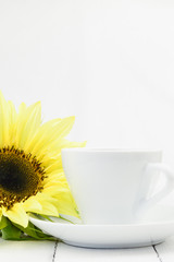 Sunflower beside coffee cup, vertical, white background.
