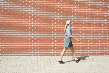 Fototapeta na wymiar Young successful business woman walking against brick wall 