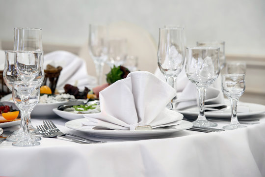 Served food and dishes for table persons. Classic simple design dining holiday table. White tablecloth with white napkins and Cutlery.