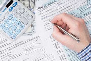 Businessman filling out USA Tax 1040 Form with calculator neat it
