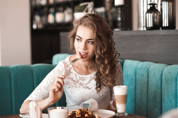 Beautiful blonde woman 20-24 year eating brownie dessert and drinking coffee in cafe. Looking away.