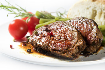 grilled lamb steak with green beans, tomatoes and bread on a white plate