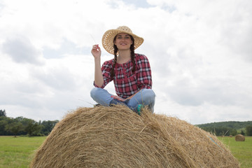 Naklejka na ściany i meble Beautiful brunette woman sitting on hay bale in warm summer day