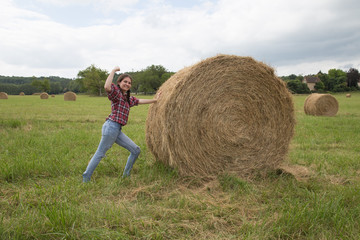 Naklejka na ściany i meble Smiling woman pushing the haystack and having fun by harvest. Country concept.