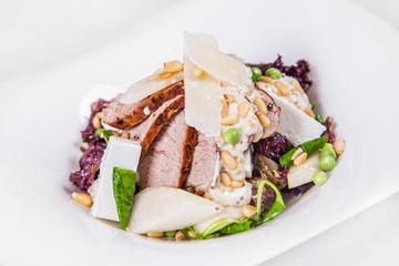 Salad with pieces of delicious homemade smoked pork ham, beans, peas, asparagus, cauliflower flavored with sauce, cheese and slices of melon. Isolated dish on a white background
