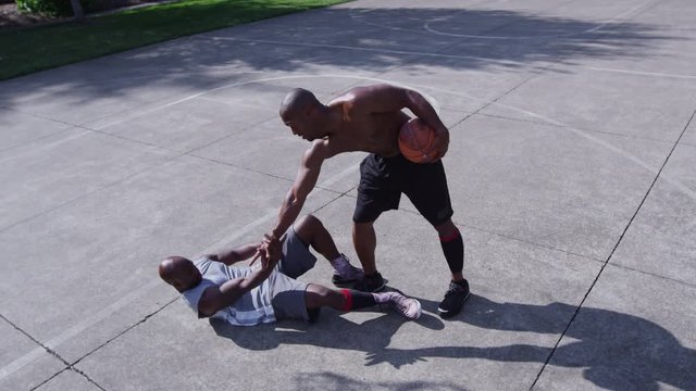 One on one street basketball; player helps rival up off court