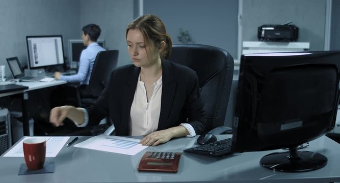 4K: Zwei Büroangestellte arbeiten in einem Büro. Die junge Frau kontrolliert gelassen Dokumente und trinkt Kaffee. Die ältere Frau regt sich heftig auf, telefoniert und verlässt wütend den Raum.