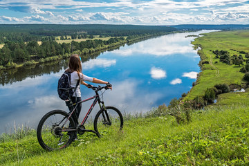 Girl rides a bicycle along the shore of the river