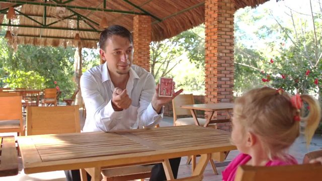 Conjurer Shows Card Pack Trick to Little Girl at Table