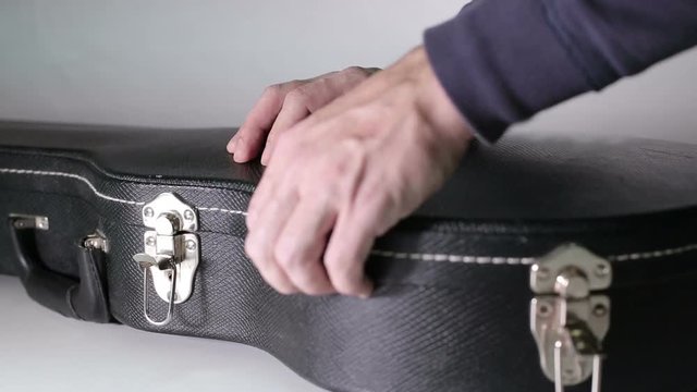 Man's hands open a case and takes a guitar out of a case.