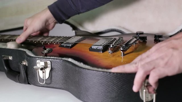 A man puts a guitar into the case.