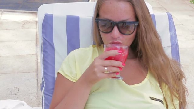 Beautiful girl drinking fruit juice while sitting by the pool