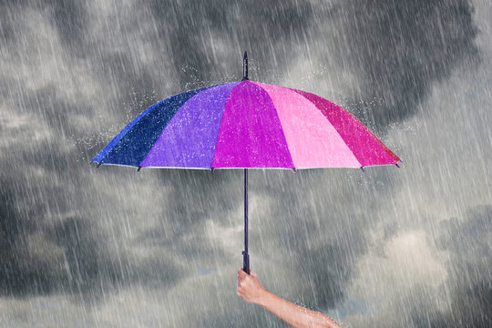hand holding multicolored umbrella under dark sky with rain