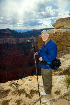Senior Man Stands on the North Rim of the Grand Canyon Taking Pi