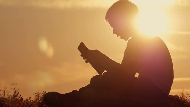 Man silhouette sitting under tree with tablet on cloudy day outdoor