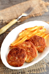 Minced meat cutlets and fries on a plate, fork and burlap on old wood background. Cutlets made with Turkey fillets and fried in vegetable oil. Recipe photo. Closeup 