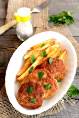 Fried meat cutlets served with fries. Turkey fillet cutlets with fries on the plate. Fork, salt shaker, fresh parsley on an old wooden background. Lunch or dinner menu. Closeup 