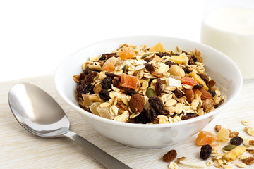 Breakfast bowl of fruit and nut muesli with milk and spoon. 