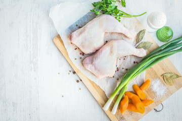 Raw chicken legs with vegetables and spices arranged on a cutting wooden board. White wood rustic background.