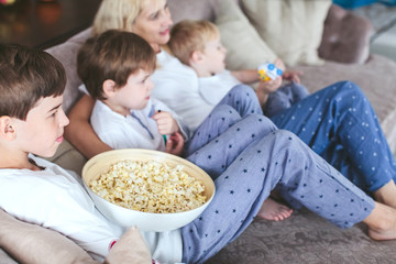 mother and sons are sitting on the couch watching television with popcorn in the kitchen