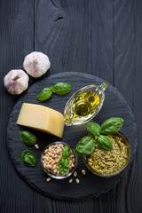 Basil pesto and its ingredients on a black wooden background