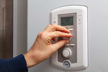 Men hand regulate temperature on 50 degree in control panel of central heating.