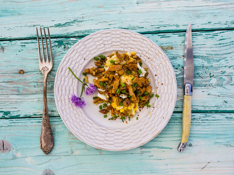 Delicious scrambled eggs with chantarelle mushrooms and chives on a wooden background.