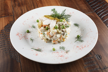 Olivier salad with chicken in a white plate. Wooden background