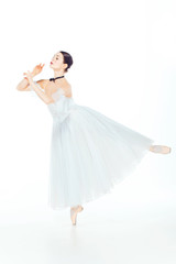 Ballerina in white dress posing on pointe shoes, studio background.
