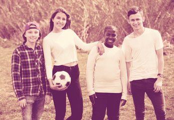 Portrait of four friends posing on countryside field with ball