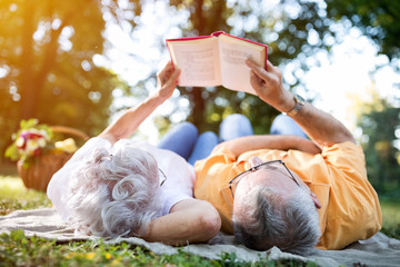 Senior couple resting at park, reading a book