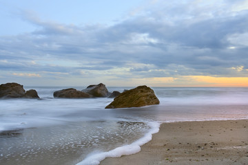 Beach at sunset (sunrise) beautiful sky with clouds. waves run ashore, taken on a long exposure, the ripples on the water and foam left a drawing in the sand. waves and mist shrouded misty water. 
