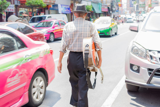 Old man walking on the street holding a guitar.