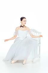 Fototapeta na wymiar Ballerina in white dress sitting, studio background.