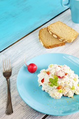 Cottage cheese with radish on a blue plate, healthy breakfast on rustic wooden table.