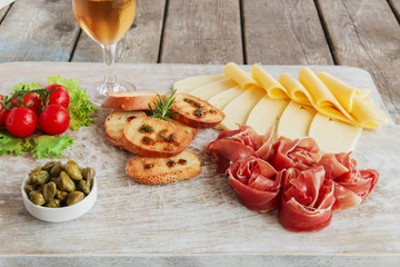 delicious appetizer to wine - ham,prosciutto, cheese, capers, tomato, served on a light wooden board