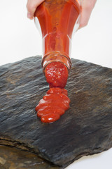 Tomato ketchup and ketchup bottle puring ketcup on a stone