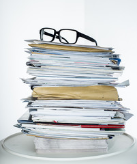 A pile of paper, envelopes, reports, letters on a table with glasses on top
