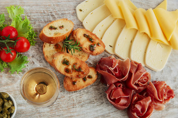 Obraz na płótnie Canvas delicious appetizer to wine - ham,prosciutto, cheese, capers, tomato, served on a light wooden board