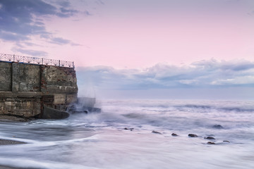 Ruins of an old brick wall destroyed by the sea. Waves beating against the wall. The sea, a soft haze, gentle colors at sunrise, sunset, fog. Solitary lonely place
