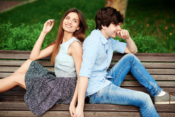 Young couple sitting on a bench in the park in summer, chatting, laughing and holding hands