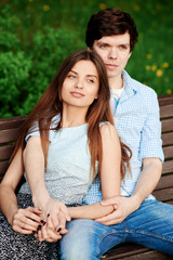 Naklejka premium Young couple sitting on a bench in the park in the summer and hugging