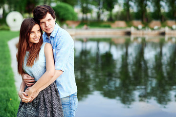 Young couple standing on the shore of the lake in the summer and hugs